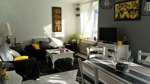 A living room with a sofa, coffee table, TV, and dining area. - Vacation Home (Loctudy)