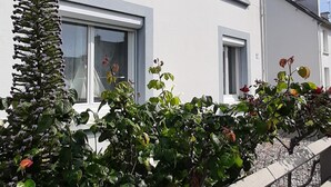 A two-story building with white exterior walls, multiple windows, and a concrete retaining wall with greenery. - Vacation Home (Loctudy)