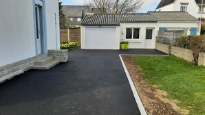 A paved driveway leading to a garage, a grassy area with a fence, and a building with a tiled roof. - Vacation Home (Loctudy)