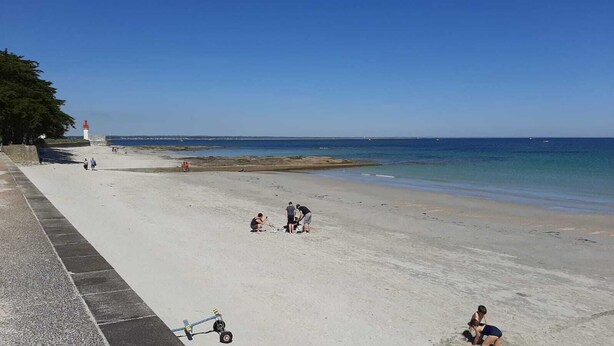 A beach with a lighthouse, a paved walkway, and a few people. - Vacation Home (Loctudy)