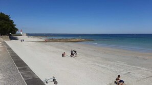Uma praia com um farol, um calçadão e algumas pessoas.