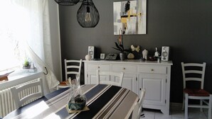 A dining area with a table, chairs, a white cabinet, and a wall-mounted abstract painting. - Vacation Home (Loctudy)