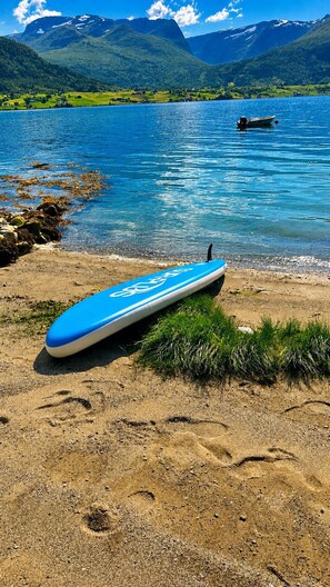 A blue surfboard on a sandy beach with a lake and mountains in the background.