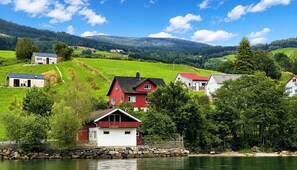 Une propriété au bord du lac, avec une maison rouge, une maison blanche et un petit chalet, le tout entouré de verdure et de collines.