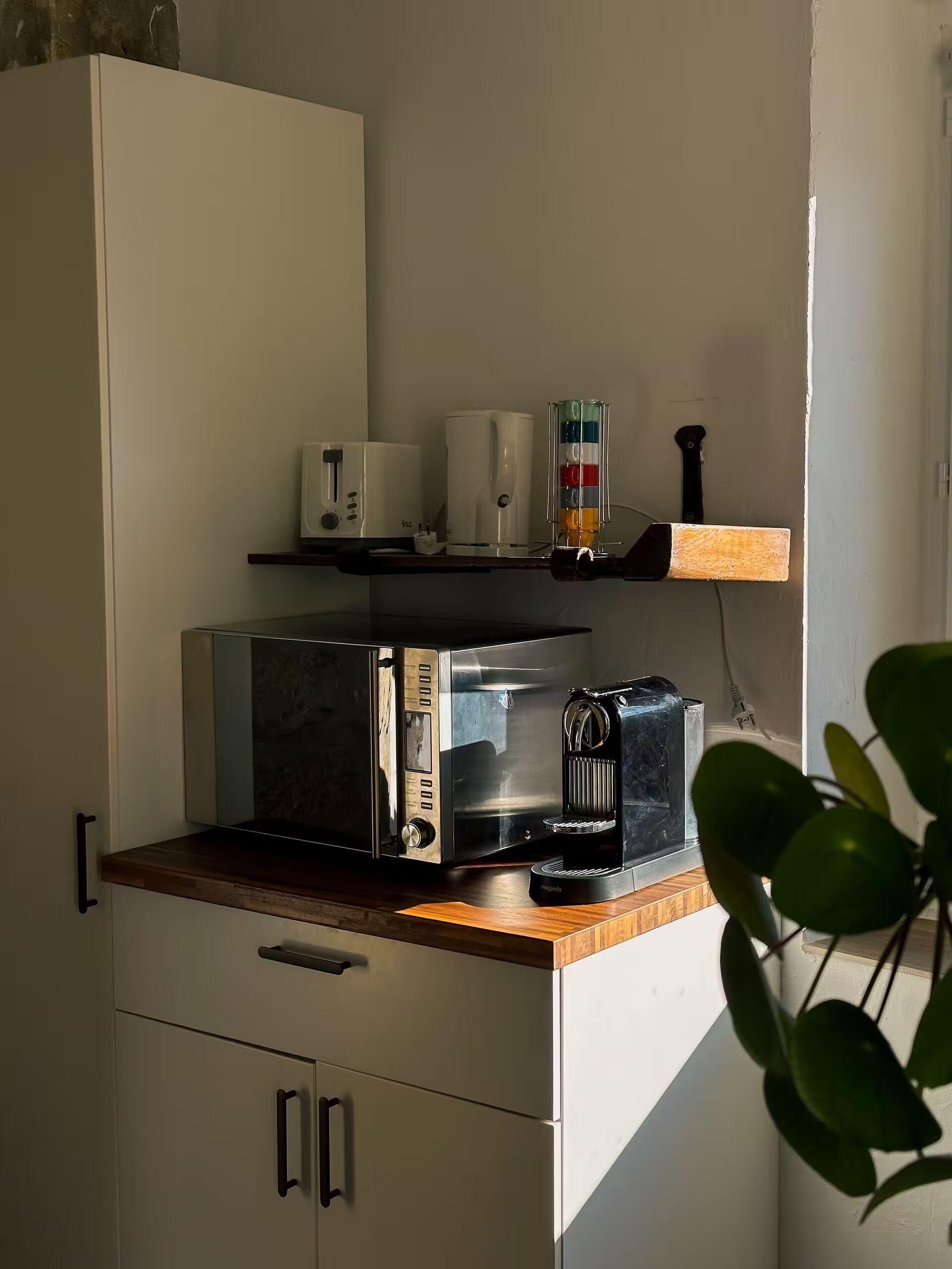 Een kitchenette met een magnetron, koffiezetapparaat en een klein plankje met een plant.
