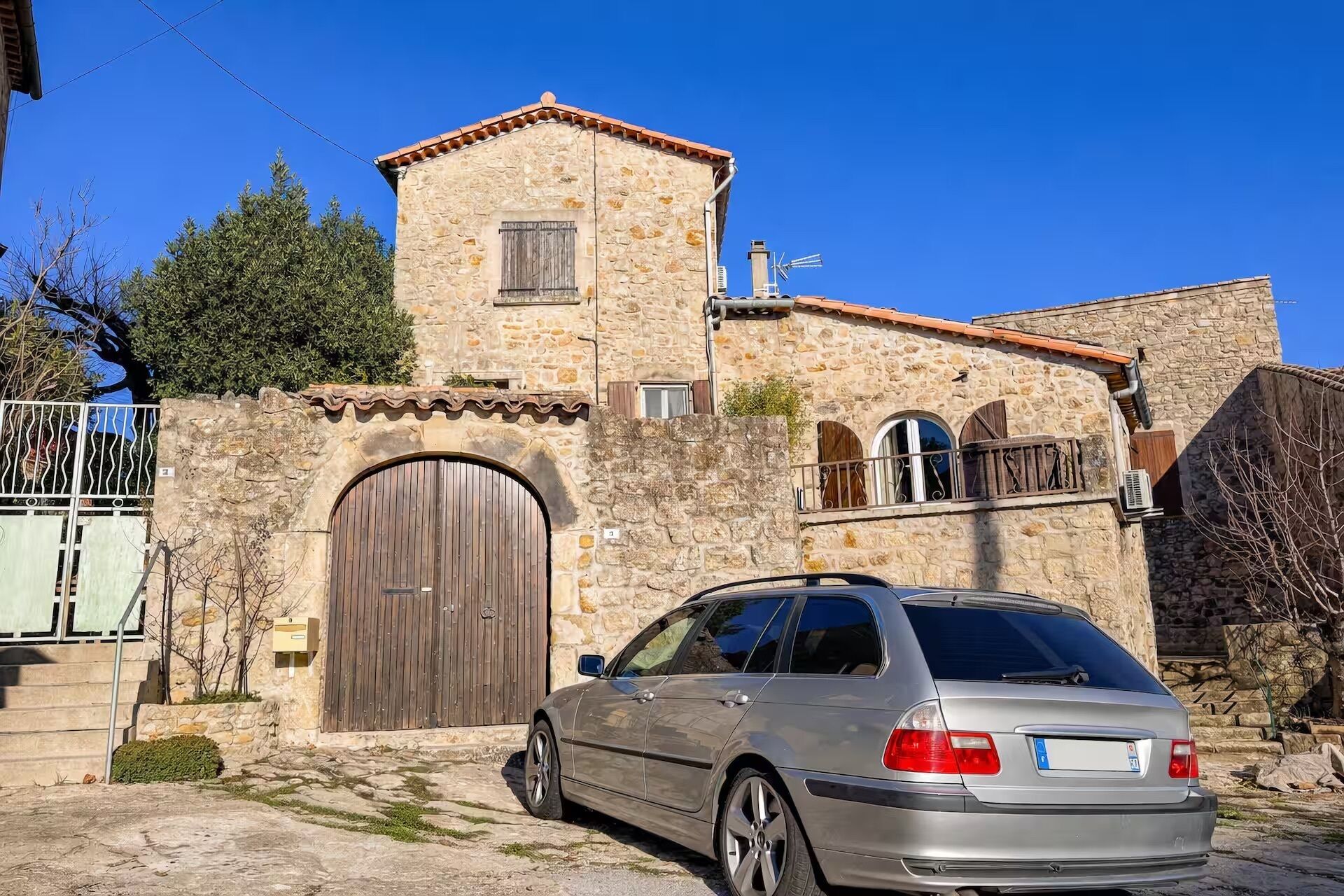 Un bâtiment en pierre avec une grande porte en bois, une petite tour et une voiture garée devant.