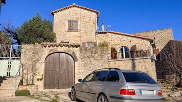 Un bâtiment en pierre avec une grande porte en bois, une petite tour et une voiture garée devant.