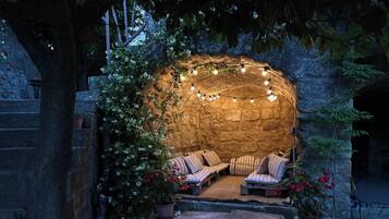 Un espace extérieur aménagé avec des murs en pierre, des guirlandes lumineuses et des plantes en pot.