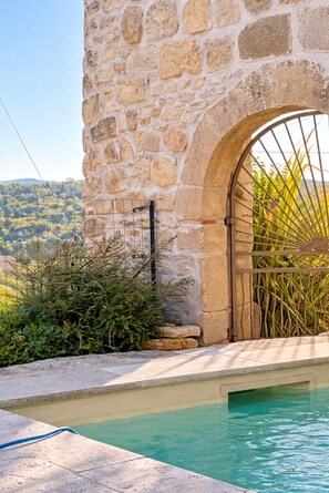 Un mur de pierre avec un portail en métal, une piscine et une vue sur un paysage vallonné.