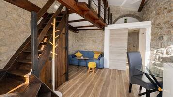 Un intérieur rustique avec un escalier en bois, un mur en pierre, un canapé bleu et une table en verre.