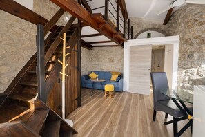 Un intérieur rustique avec un escalier en bois, un mur en pierre, un canapé bleu et une table en verre.