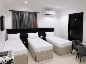 A hotel room with two single beds, a bedside table with a lamp, a chair, a small table with a decorative item, and an air conditioning unit on the wall. - فندق جنة الشعب (Makkah)