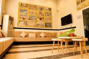 A living room with a sofa, a coffee table with plants, a wall-mounted TV, and a large photo collage. - فندق جنة الشعب (Makkah)