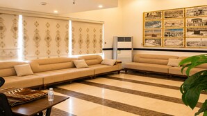 Un vestíbulo de hotel con un conjunto de sofás, una mesa con una botella de agua, un muro con estampado y una pared de fotografías enmarcadas.