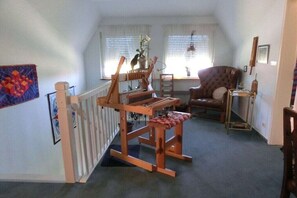 Ein Zimmer mit einem Holzschaukelstuhl, einem kleinen Tisch mit einer Vase und einem Fenster mit Jalousien.
