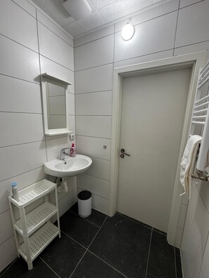 Ein Badezimmer mit weiß gefliesten Wänden, einem weißen Waschbecken mit Spiegel darüber, einem weißen Handtuchhalter und einer weißen Tür.