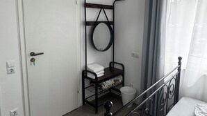 Une chambre à coucher avec un lit, une étagère en métal, une porte blanche et une fenêtre avec des rideaux.
