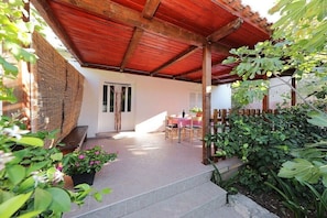 Ein überdachter Patio-Bereich mit Tisch und Stühlen, einem Holzzaun und Topfpflanzen.