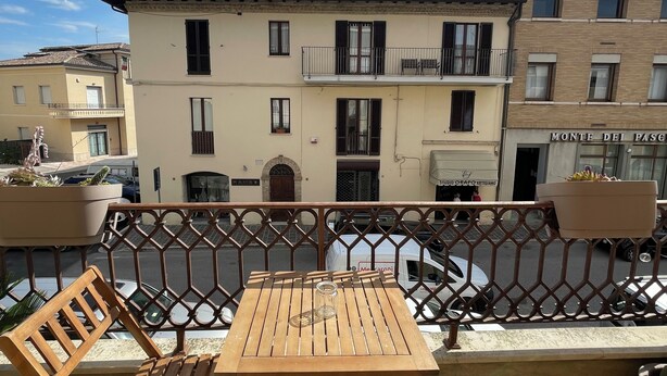 Een balkon met een houten tafel en stoelen, uitzicht op gebouwen en een heldere lucht.