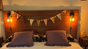 Een bed met een houten hoofdbord, twee kussens, een lichtslingering en een nachtkastje met een lamp.