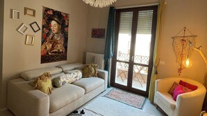 Een woonkamer met een bank, een kamerkleed met dessin, een hanglamp en een deur naar een buitenruimte.