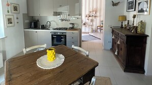 Een eetgedeelte met een houten tafel en stoelen, een keuken op de achtergrond en zicht op een andere kamer.
