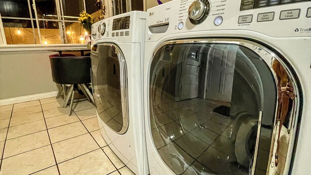 A laundry area with two front-loading washing machines, a window with a view of the outside, and a small table with chairs. - Beverlywood Apt Master Suite - Private Bath & Production Studio (Los Angeles)