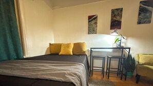 A bedroom with a bed, a desk, two chairs, a green plant, and artwork on the wall. - Beverlywood Apt Master Suite - Private Bath & Production Studio (Los Angeles)
