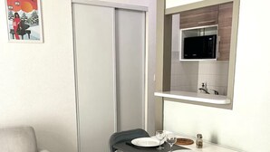 Um espaço de estar compacto com área de jantar, um sofá com almofada vermelha, micro-ondas e um quadro na parede.