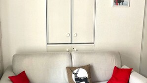 Sala de estar com sofá, duas almofadas vermelhas, almofada em formato de veado, cabeça de veado de madeira, um armário e um quadro emoldurado.