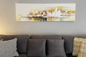 Ein graues Sofa mit gemusterten Kissen und einem Stadtbild darüber.