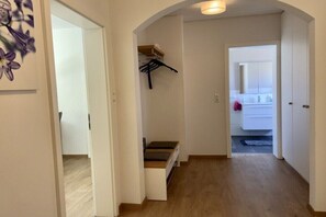 Ein Flur mit Holzboden, einer Treppe und einer Tür zu einem Badezimmer mit Spiegel und Schränken.