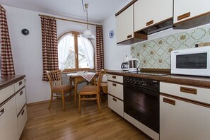 A compact kitchen with a dining table, chairs, a microwave, and a stove. - Holiday apartment with 1 bedroom (Bad Kohlgrub)