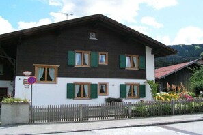 Ein zweigeschossiges Gebäude mit grünen Fensterläden, einer weißen Fassade und einem Holzzaun.