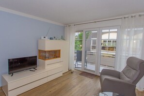Ein modernes Wohnzimmer mit Flachbildfernseher, einer Vitrine und einem grauen Sofa, sowie einer Glastür zu einem Außenbereich.