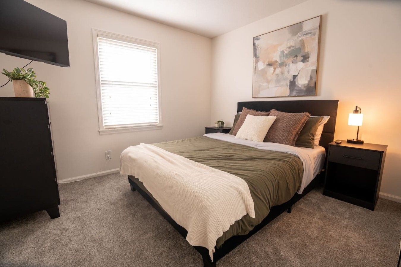 A bedroom with a bed, bedside table, lamp, and a painting on the wall.
