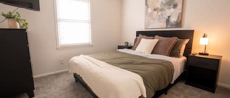 A bedroom with a bed, bedside table, lamp, and a painting on the wall.