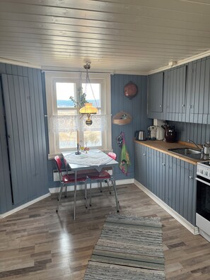 A kitchen with wooden cabinets, a dining table with chairs, a hanging lamp, and a view through a window.