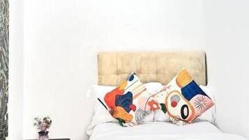 A bedroom with a bed, two pillows with a colorful design, a nightstand with a small plant, and a headboard.