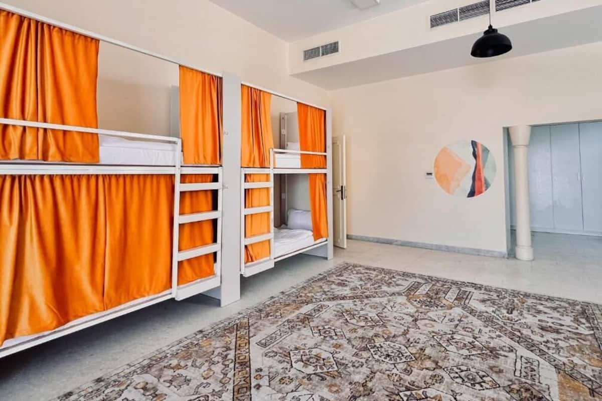 A room with bunk beds, orange curtains, a patterned rug, and a ceiling fan.