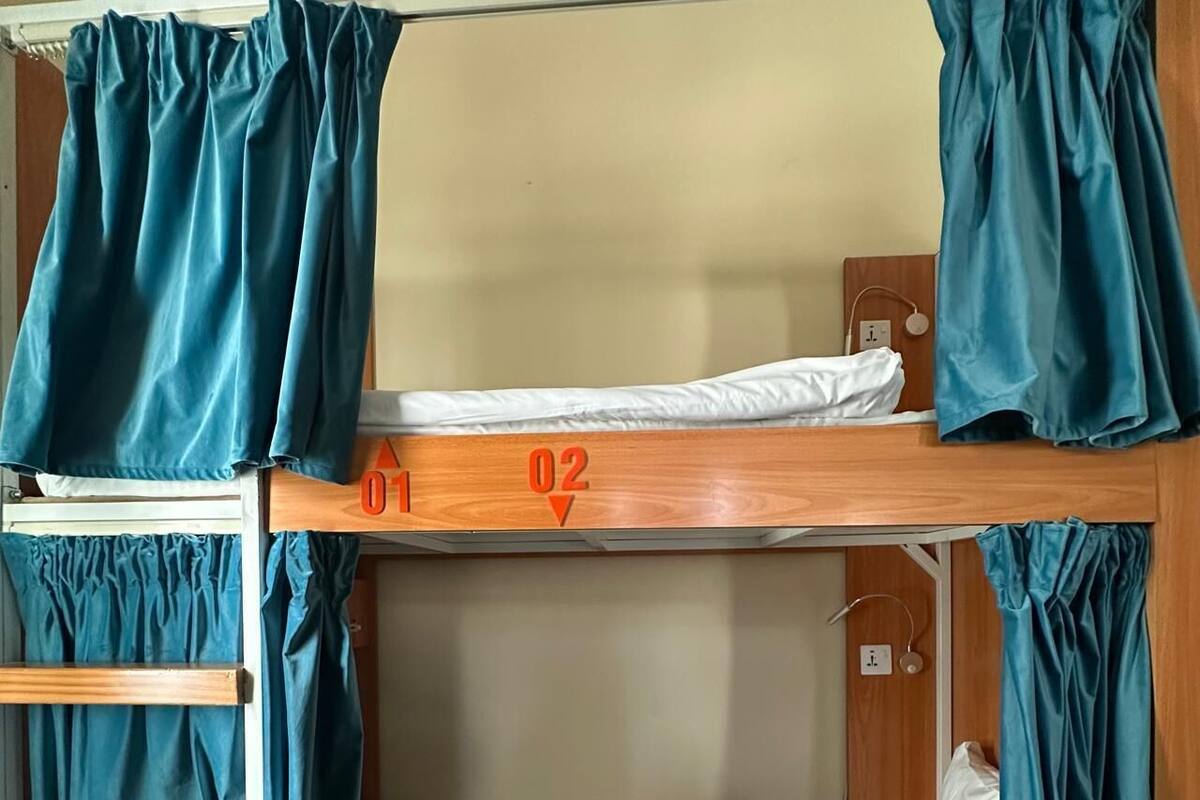 A bunk bed with two levels, a wooden ladder, and curtains.