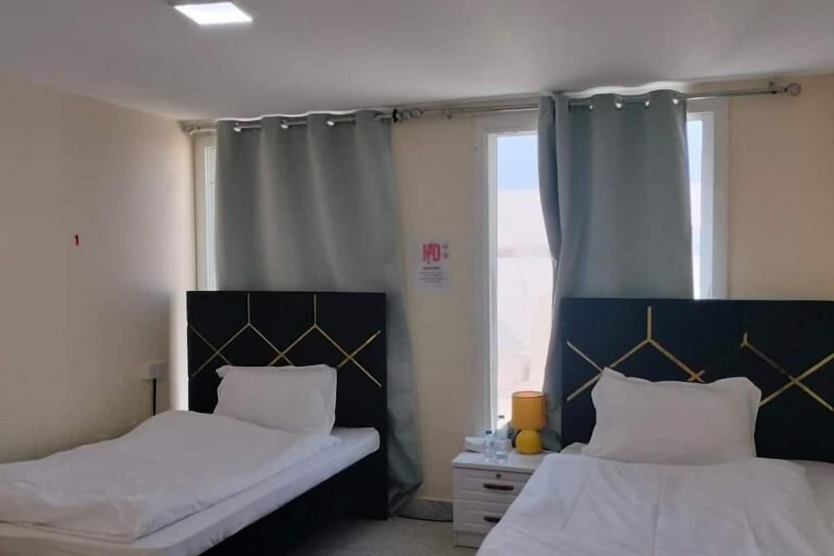 A room with two single beds, a nightstand with a lamp, and a window with curtains.