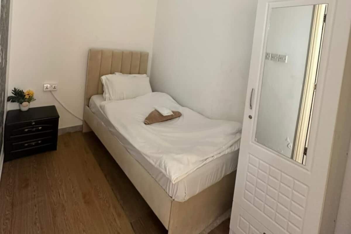 A bedroom with a bed, a wardrobe, a nightstand, and a ceiling vent.