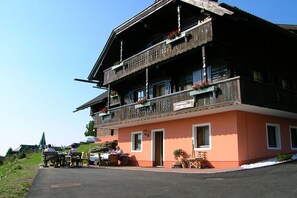Ein traditionelles Holzhaus mit Balkon, einem Schild das auf ein Restaurant hinweist und Außenplätzen.