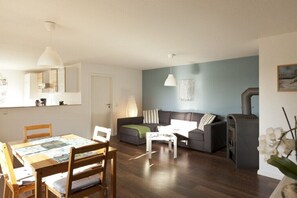 Ein Wohnzimmer mit einer Couch, einem Esstisch mit Stühlen, einem Couchtisch, einem Kamin und einer Hängelampe.