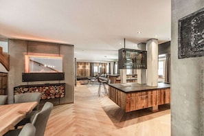 A modern kitchen with a central island, a built-in fireplace, and a dining area with a herringbone floor pattern. - At Franzerl am Weissensee (Weissensee)