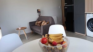 Moderni olohuone, jossa on pyöreä pöytä, sohva, pesukone ja pieni keittiötila.