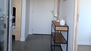 Käytävä, jossa on puinen ovi, valkoinen seinä, puinen hylly, jossa on lamppu, ja kattovalaisin.