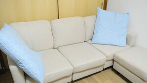 Un canapé d’angle beige, agrémenté de deux coussins bleu clair, est placé contre un mur en bois et sur un plancher en bois.