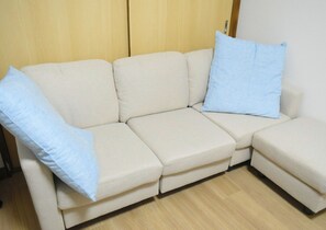 A beige sectional sofa with two light blue pillows against a wooden wall and a wooden floor.